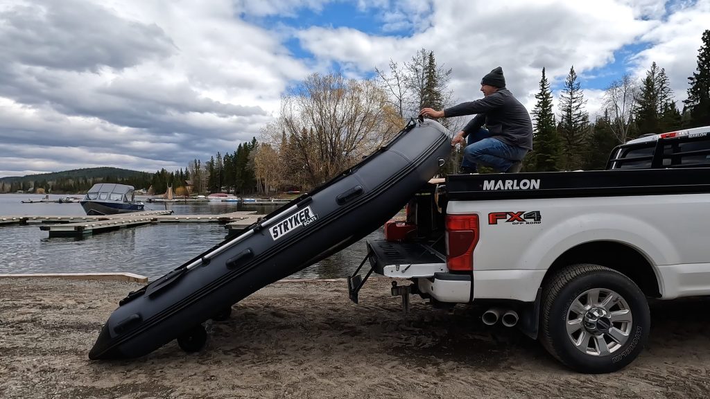 man pulling an inflatable boat onto a sled deck of a truck
