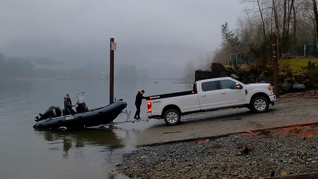 white ford with inflatable rigid hull boat in trailer launching into river side view